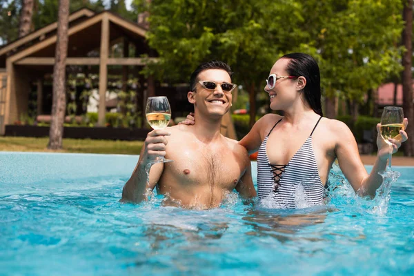 Casal com copos de vinho sorrindo na piscina ao ar livre — Fotografia de Stock