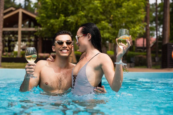 Woman hugging happy boyfriend with wine in swimming pool — Stock Photo