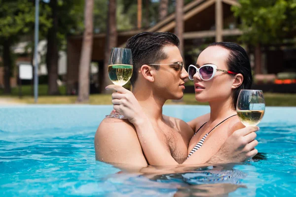 Homem de óculos de sol beijando namorada com vinho na piscina — Fotografia de Stock