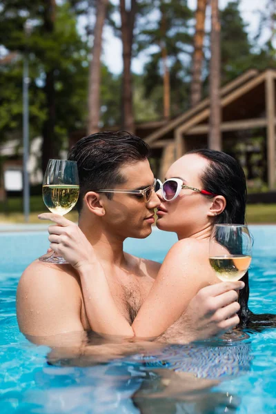 Casal em óculos de sol beijando enquanto descansa com vinho na piscina — Fotografia de Stock