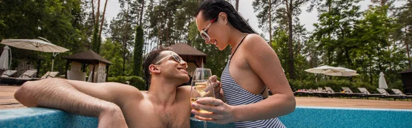 Donna sorridente che tiene un bicchiere di vino vicino a bordo piscina e fidanzato sul resort, banner — Foto stock