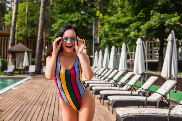 Захоплена жінка в купальнику і сонцезахисних окулярах стоїть на відкритому повітрі — стокове фото