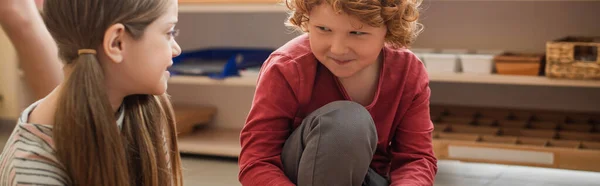 Rossa ragazzo sorridente mentre guarda la ragazza nella scuola montessori, banner — Foto stock