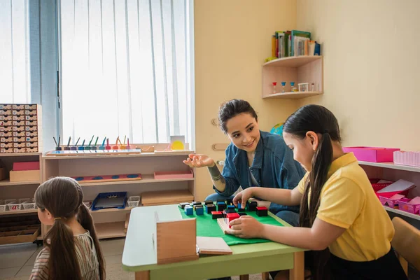 Sorridente professor gestos enquanto jogar multicolorido cubos jogo com menina asiática — Fotografia de Stock