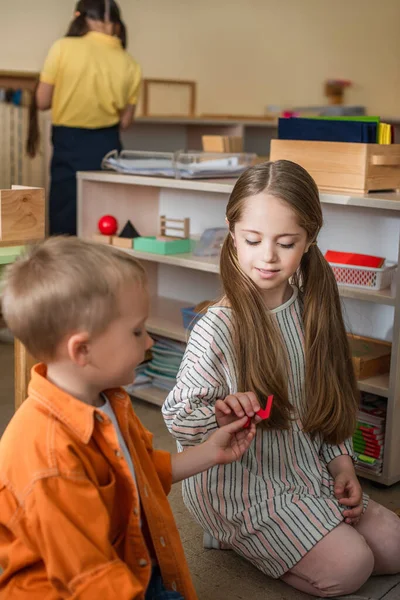 Garçon donnant élément de puzzle pour fille assis sur le sol dans l'école montessori — Photo de stock