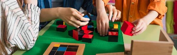 Vista parcial de niño y maestro jugando con cubos de madera en la escuela montessori, pancarta - foto de stock