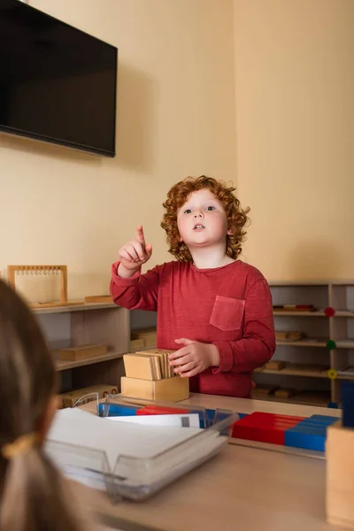 Ragazzo rosso che punta con il dito vicino a carte di legno e ragazza in primo piano sfocato — Foto stock