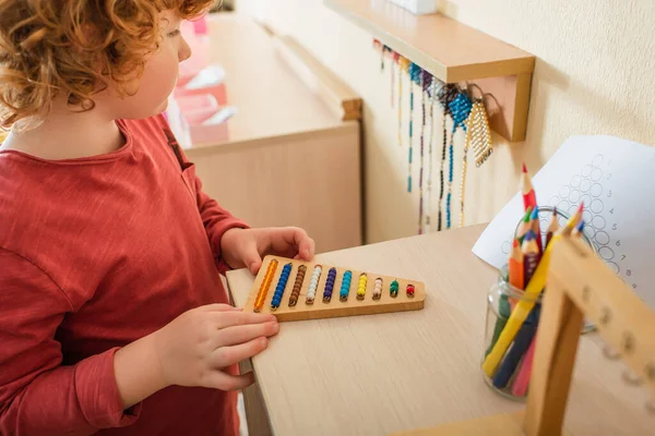 Vue recadrée d'enfant jouant jeu de perles multicolores près de crayons de couleur flous — Photo de stock