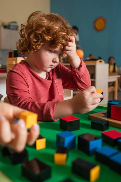 Nachdenklicher Junge spielt in Montessori-Schule mit bunten Blöcken auf verschwommenem Vordergrund — Stockfoto