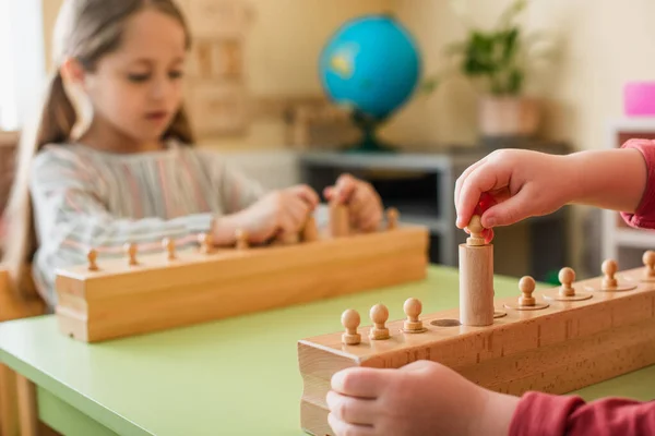 Menino jogando jogo com elementos de madeira perto menina borrada na escola montessori — Fotografia de Stock