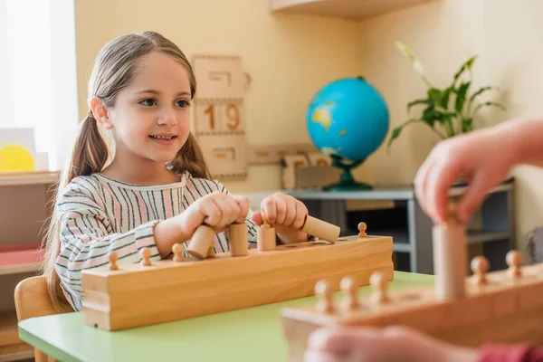 Sorridente ragazza giocando gioco educativo con elementi di legno vicino ragazzo sfocato — Foto stock