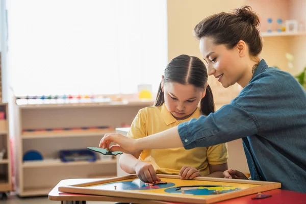 Junge Lehrerin und asiatisches Mädchen kombinieren Erdkartenpuzzle in Montessori-Schule — Stockfoto