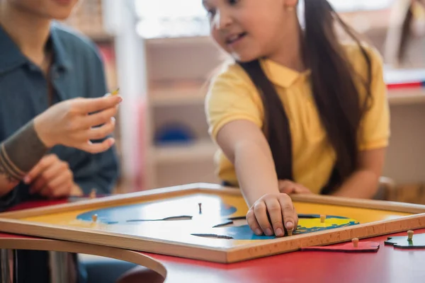 Cropped view of asian girl combining earth map puzzle near teacher, blurred background — Stock Photo