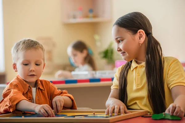 Asiatico ragazza sorridente mentre combinazione mondo mappa puzzle con ragazzo in montessori scuola — Foto stock