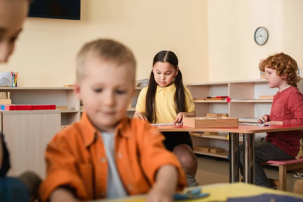Interracial kids playing educational game near boy and teacher on blurred foreground — Stock Photo