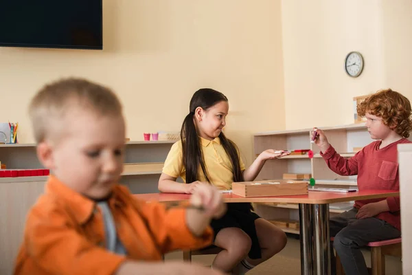 Asiático chica jugando educativo juego en aula cerca chico en borrosa primer plano - foto de stock