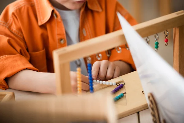 Partial view of kid playing colorful beads game on blurred foreground — Stock Photo