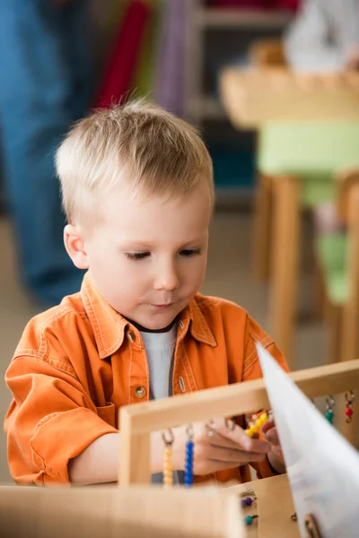 Niño contando cuentas de colores mientras juega juego educativo en la escuela montessori - foto de stock