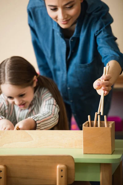 Insegnante sorridente che prende bastoni di legno mentre il bambino gioca a scuola montessori — Foto stock