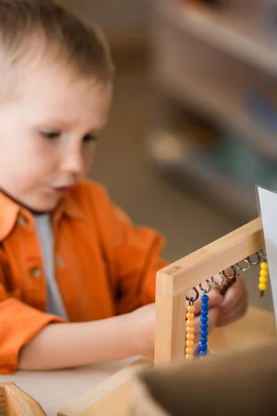 Garçon flou jouant jeu de perles en bois à l'école montessori — Photo de stock