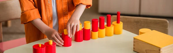 Vue recadrée du gamin jouant avec des cylindres rouges et hurlants à l'école montessori, bannière — Photo de stock