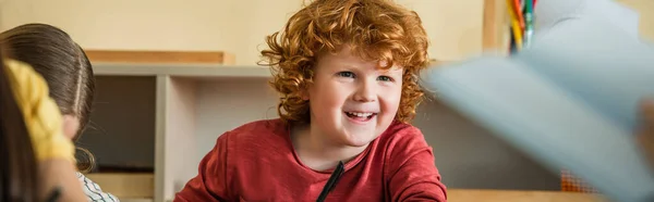 Rosso ragazzo sorridente vicino ragazza in montessori scuola su sfocato primo piano, striscione — Foto stock