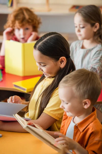 Multiethnic kids reading books in classroom on blurred background — Stock Photo