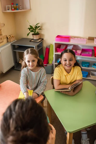 Joyeuses filles multiethniques regardant l'enseignant sur le premier plan flou pendant la leçon — Photo de stock