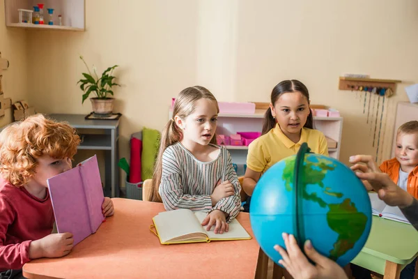 Montessori insegnante di scuola che mostra il globo ai bambini multiculturali durante la lezione — Foto stock