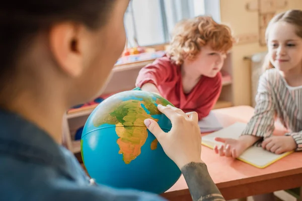 Selektiver Fokus des Globus in den Händen des Lehrers in der Nähe von Kindern in der Montessori-Schule — Stockfoto