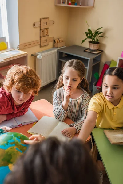 Blurred teacher pointing at globe near multiethnic friends during lesson — Stock Photo