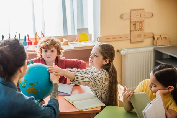 Mädchen berührt Globus nahe Lehrer und multiethnischen Kindern in Montessori-Schule — Stockfoto