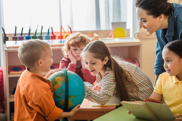 Erstaunt Mädchen Blick auf Globus in der Nähe interracial Freunde und Lehrer — Stockfoto