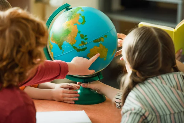 Vista posteriore del ragazzo offuscata che punta al globo vicino ai bambini e insegnante — Foto stock