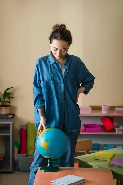 Montessori school teacher looking at globe in classroom — Stock Photo