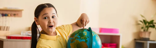 Astonished asian child pointing at globe while looking at camera, banner — Stock Photo