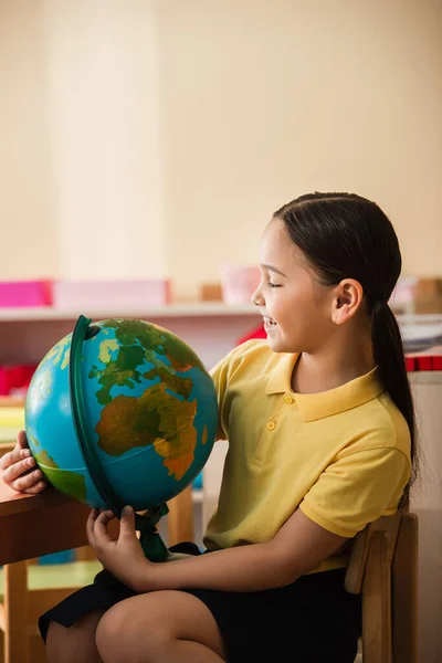 Glücklich asiatische Mädchen Blick auf Globus in Montessori-Schule — Stockfoto