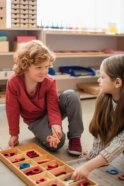 Children looking at each other while playing with wooden letters on floor — Stock Photo