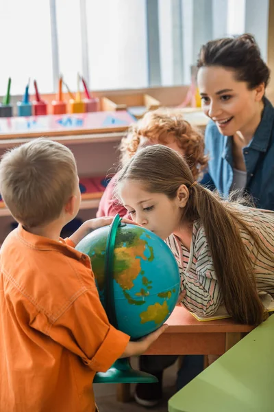 Neugieriges Mädchen blickt auf Globus in der Nähe von Kindern und verschwommener Lehrer im Klassenzimmer — Stockfoto