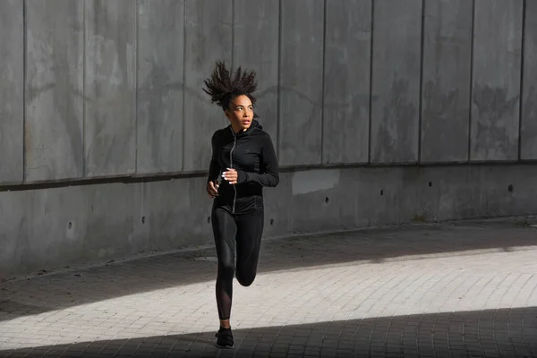 Young african american sportswoman running near building on urban street — Stock Photo