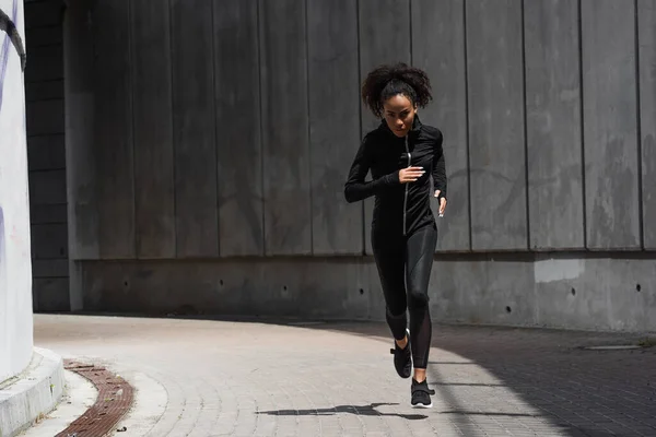 Jovem afro-americana olhando para a câmera enquanto jogging na rua urbana — Fotografia de Stock