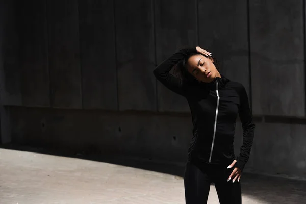 Young african american sportswoman with closed eyes stretching neck outdoors — Stock Photo