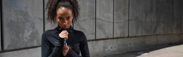 Afroamerikanische Sportlerin blickt in die Kamera, während sie draußen Sportjacke reißt, Banner — Stockfoto