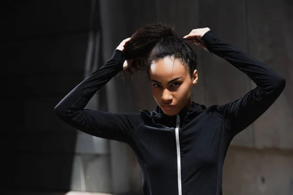 Jeune sportive afro-américaine ajustant les cheveux dans la rue urbaine — Photo de stock