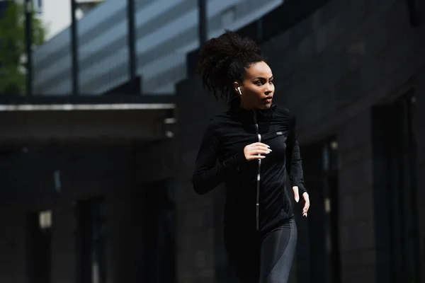 African american woman in earphone jogging on urban street — Stock Photo