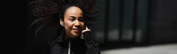 Alegre afroamericana deportista en auriculares corriendo al aire libre, pancarta - foto de stock