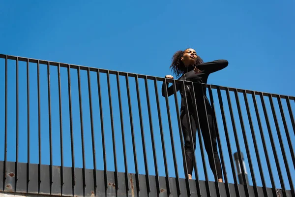 Low angle view of african american sportswoman in earphone stretching on bridge — Stock Photo