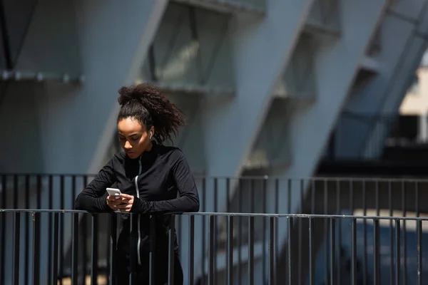 Sportiva afroamericana in auricolare utilizzando smartphone su strada urbana — Foto stock