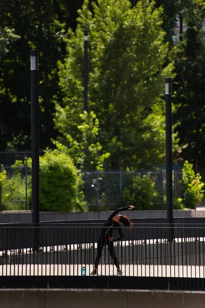 Giovane sportiva afro-americana piegandosi mentre si allena sul ponte — Foto stock