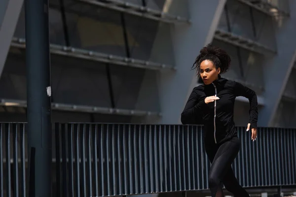Desportista afro-americana de jaqueta esportiva correndo na rua urbana — Fotografia de Stock